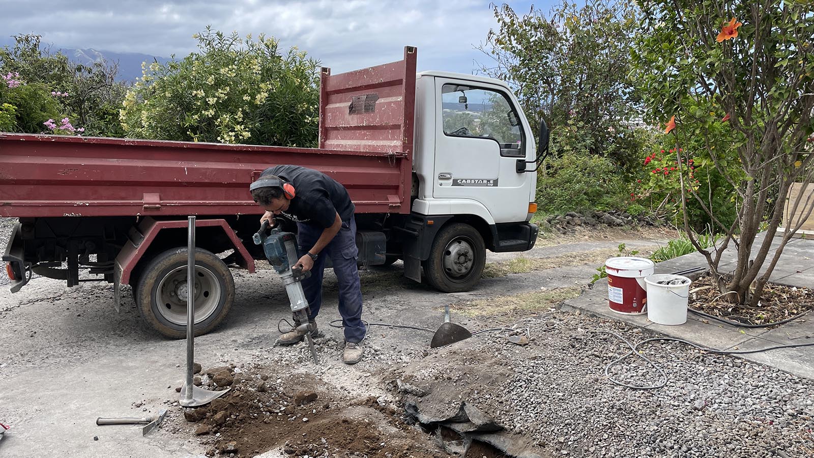 Miguel boort een gat om de aanvoer van het gemeentewater, die nu nog los ligt, straks veilig onder het beton te kunnen leggen